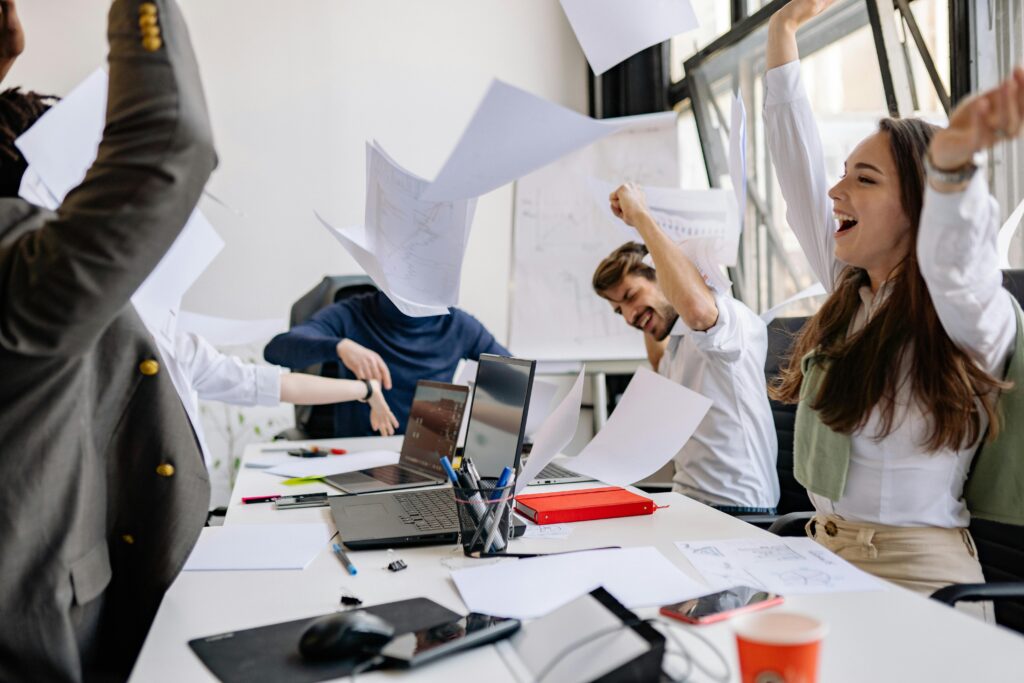 Group of diverse business professionals celebrating success in a modern office setting.